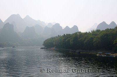 Tour boats on the Li River Guangxi China with karst dome mountains in the haze