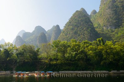 Tour boat rafts on the Li River Guangxi China with karst dome mountains in the haze