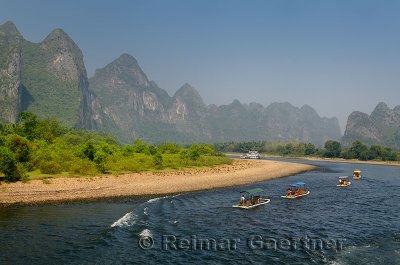 Row of tour boat rafts and a cruise ship heading up the Li river China with karst mountains