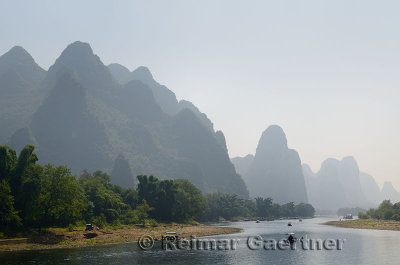 Tour boat rafts heading down the Li river Guangxi China with tall karst mountain cones in haze