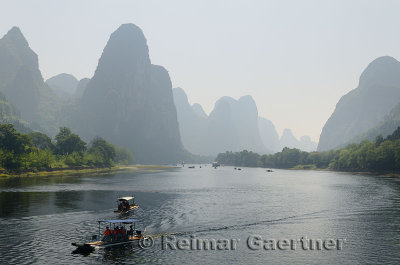 Tour boat rafts on the Li river Guangxi China with tall karst mountain peaks receding in the haze