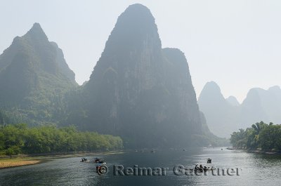 Tour boat rafts on the Li river Guangxi China with sugarcone karst mountain peaks receding in the haze