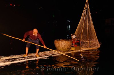 Chinese fisherman lifting Cormorant with fish onto the raft on the Li river in Yangshuo China at night
