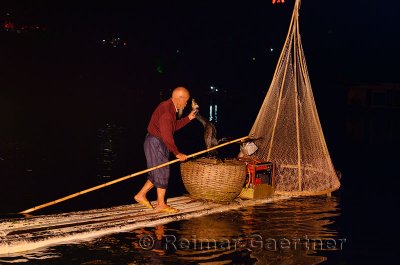 Chinese night fisherman lifting Cormorant with fish into a basket on the Li river in Yangshuo China