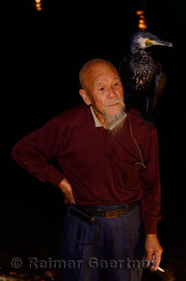 Smoking Chinese fisherman with a trained Great Cormorant on the shoulder at night on the Li river in Yangshuo China