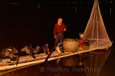 Chinese fisherman with cormorants and net on a raft in Yangshuo China at night on the Li river