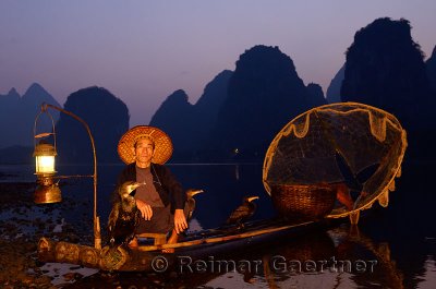 Fisherman with cormorants on bamboo raft at dawn on the shore of the Li river Yangshuo China