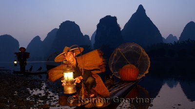 Cormorant fisherman tending lantern with birds on bamboo raft at dawn on the shore of the Li river Yangshuo China