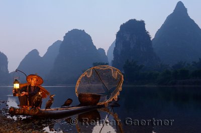 Cormorant fisherman lighting lamp with birds on bamboo raft at dawn on the shore of the Li river Yangshuo China