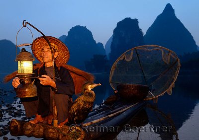 Fisherman with lantern on a bamboo raft with cormorants at dawn on the shore of the Li river Yangshuo China