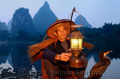 Cormorant fisherman with lamp and bird on bamboo raft at dawn on the shore of the Li river Yangshuo China