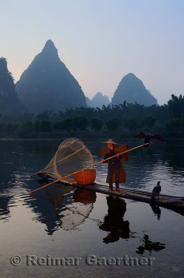 Cormorant fisherman polling down the Li river Yangshuo China with tall karst limestone peaks at dawn