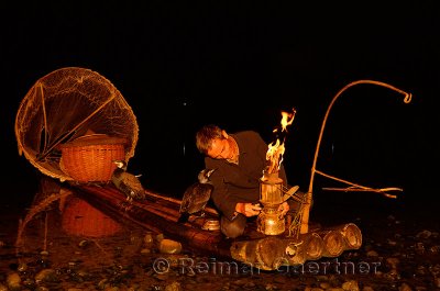 Cormorant fisherman lighting his lantern on the Li river Yangshuo China in early morning darkness