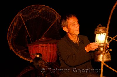 Cormorant fisherman lifting his lamp on his raft in early morning darkness on the Li river Yangshuo China