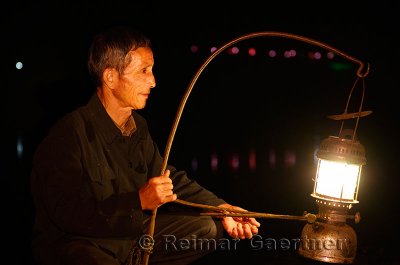 Cormorant fisherman placing his lamp on his raft in early morning darkness on the Li river Yangshuo China