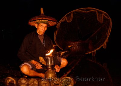 Cormorant fisherman lighting his lamp in early morning darkness on the Li river Yangshuo China