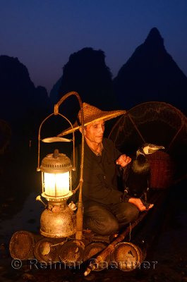 Chinese cormorant fisherman holding a bird on a bamboo raft with lantern at dawn on the Li river Yangshuo China