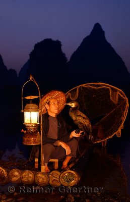 Fisherman looking at cormorant on bamboo raft with lantern and net at dawn on the Li river Yangshuo China
