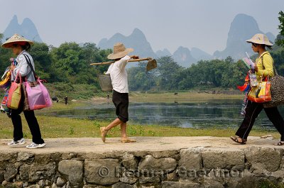 Chinese women walking on stone bridge at Fuli Li river inlet with karst mountain peaks China