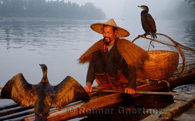 Smiling cormorant fisherman with birds on a bamboo raft on the Li river at dawn Xingping China