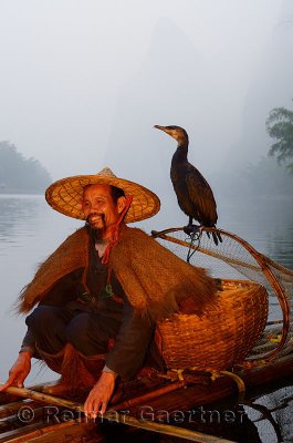 Smiling cormorant fisherman with bird on a net on the Li river at dawn with Karst mountain peaks China