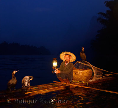 Cormorant fisherman with lamp on bamboo raft at dawn on Li river near Xingping China