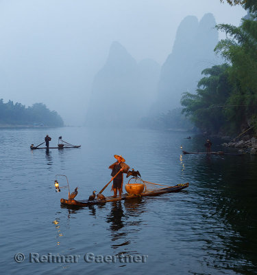 Cormorant fishermen in mist at dawn on the Li river with Karst mountain peaks near Xingping China