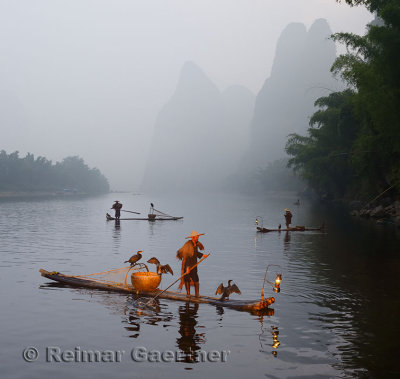 Cormorant fisherman paddling bamboo raft at dawn on the Li river with Karst mountain peaks near Xingping China