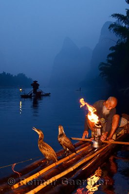 Cormorant fisherman lighting a flaming lamp on a bamboo raft at dawn on Li river near Xingping China