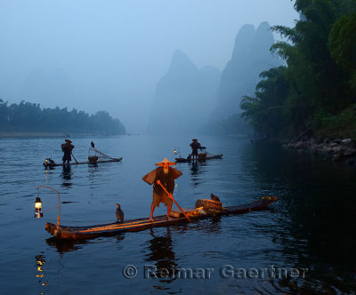 Three early morning Cormorant fishermen on bamboo rafts on Li river near Xingping China