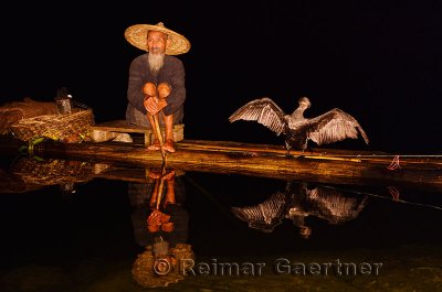 Cormorant fisherman and bird reflected in a calm Li river at night from a bamboo raft Huangbutan China
