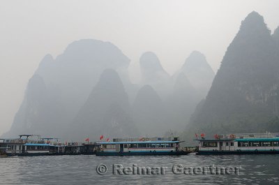 Tour boat barges on the Li river at Xingping China with Karst limestone peaks in mist