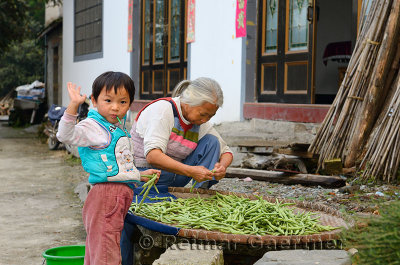 Grandson waving and Grandmother trimming beans in Shangshe village on Fengle lake Huangshan China