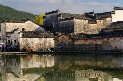Ancient buildings with geese and tourists reflected in the still Half moon pond in Hongcun village China