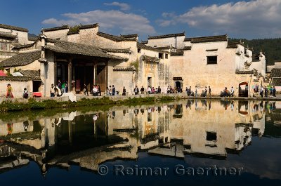 Ancient white buildings and tourists reflected in the still Half moon pond in Hongcun village China