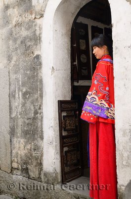 Profile of a new bride wearing her red wedding dress in the doorway of an ancient Hongcun village building China