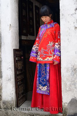 Young bride wearing her red wedding dress in the doorway of a Hongcun village building China