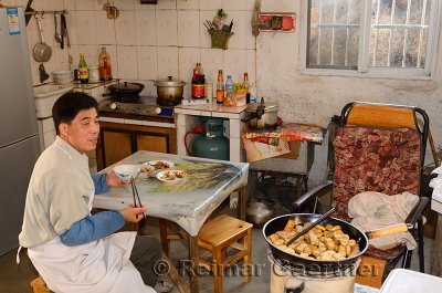 Chinese tofu worker eating lunch in the kitchen in ancient Chengkan village China