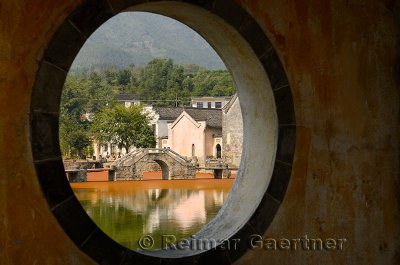 Ancient bridge on the Longxi river and Hui houses through a porthole in Chengkan village China