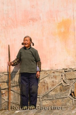 Old Chinese woman with staff leaning on wall in ancient village of Chengkan Huangshan China