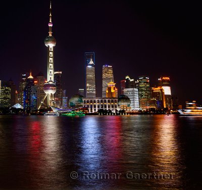 Bright night lights of Pudong high rise towers reflected in the Huangpu river with boats Shanghai China