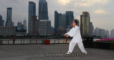Tai Chi sword master in white and kite flyer on the Bund with Pudong high rise towers in the morning Shanghai China
