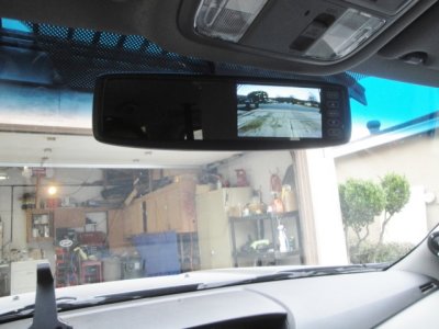 Mirror mounted in vehicle, showing rear backup camera image (automatically turns to camera in reverse)