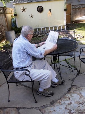 Ron reads the newspaper in the backyard.