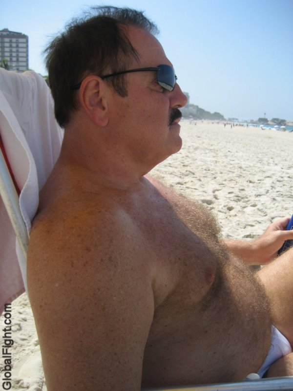 suntanning gay bear man sitting on beach hairychest.jpg