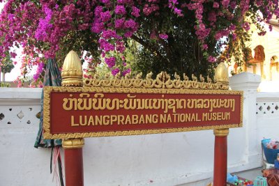 Sign for the Royal Palace (Luang Prabang National) Museum with buganvilias behind.