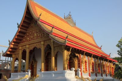 The temple is richly decorated, with fish and naga brackets supporting the roof from red and gold filigree pilasters.