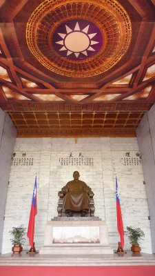 Statue of Chiang Kai-shek with flags on both sides of him and an impressive ceiling decoration.