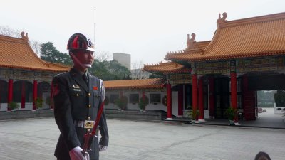 Guard standing at attention with the courtyard and Martyrs' Shrine buildings in the background.