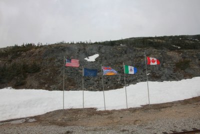 U.S., Alaskan, British, Yukon and Canadian flags at the U.S. Canadian border as seen from the train.